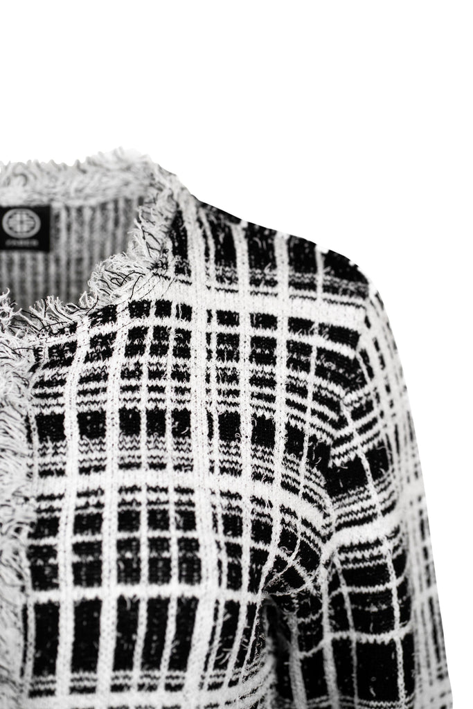 Detailansicht Schulter - Klassische Bouclé-Jacke in weiß mit schwarzem Karomuster, durchgehender Knopfleiste und dekorativen Fransenabschlüssen an Kragen, Saum und Ärmeln. Zwei kleine Pattentaschen auf Hüfthöhe unterstreichen den eleganten Look im Chanel-Stil.