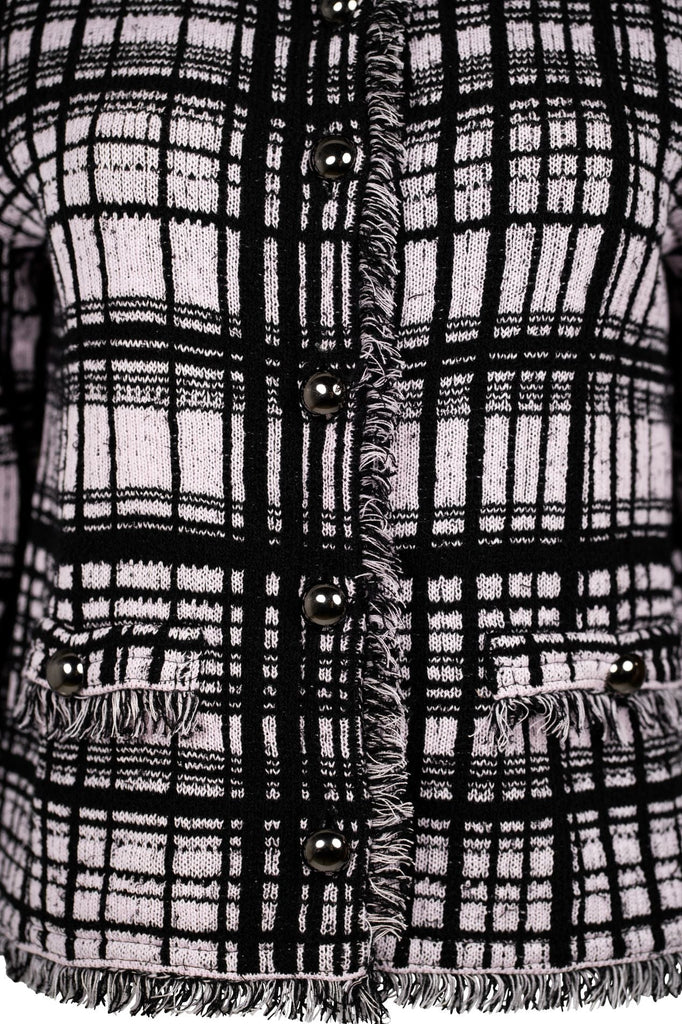 Detailansicht - Klassische Bouclé-Jacke in Rosé mit schwarzem Karomuster, durchgehender Knopfleiste und dekorativen Fransenabschlüssen an Kragen, Saum und Ärmeln. Zwei kleine Pattentaschen auf Hüfthöhe unterstreichen den eleganten Look im Chanel-Stil.