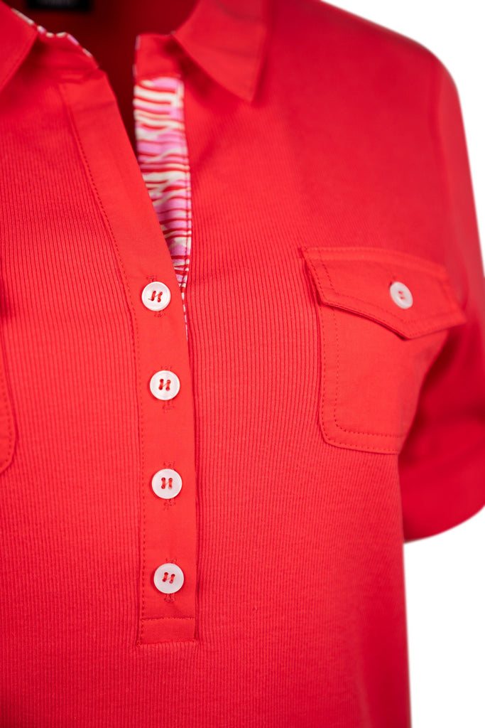 Detailansicht Kragen - Rotes Damen-Poloshirt mit halber Knopfleiste und kurzen, aufkrempelbaren Ärmeln. Zwei Brusttaschen mit Knopfklappen. Innenkragen mit rot-weißem Muster als farbiger Akzent. Sportlich und stilvoll zugleich.