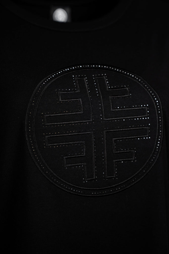 Detailansicht Logo - Schwarzes Damen-T-Shirt mit Rundhalsausschnitt und halblangen Ärmeln. Auf der Vorderseite befindet sich ein dezentes, schwarzes, kreisförmiges Faber-Logo in Ton-in-Ton-Optik mit leicht glänzender Struktur – minimalistisch und stilvoll zugleich.