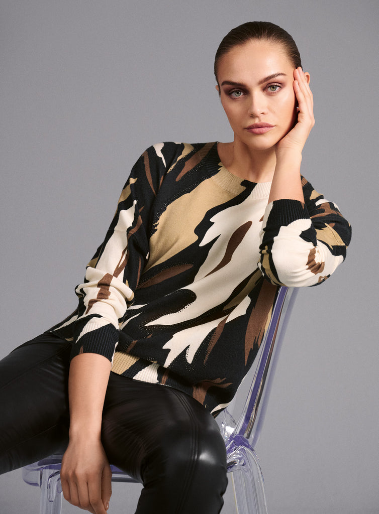 Model trägt Langarmshirt mit Rundhalsausschnitt und ausdrucksstarkem Muster in Schwarz, Braun, Camel und Weiß. Das abstrakte Design in dynamischer Linienführung verleiht dem Shirt einen modernen, künstlerischen Look.