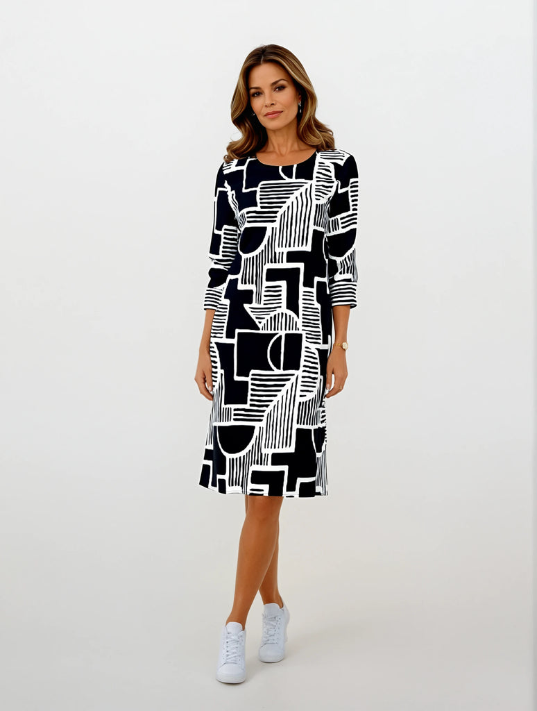 Model trägt Knielanges Damenkleid mit 3/4-Ärmeln in Dunkelblau und Weiß. Abstraktes, grafisches Muster aus Linien und geometrischen Formen. Rundhalsausschnitt, gerade Passform. Elegant und modern.
